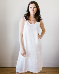 A woman standing in front of a neutral background, wearing a white sleeveless Dayna Dress in White by CP Shades.