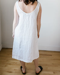 A person standing in a room wearing a white linen CP Shades Dayna Dress and black slip-on shoes.