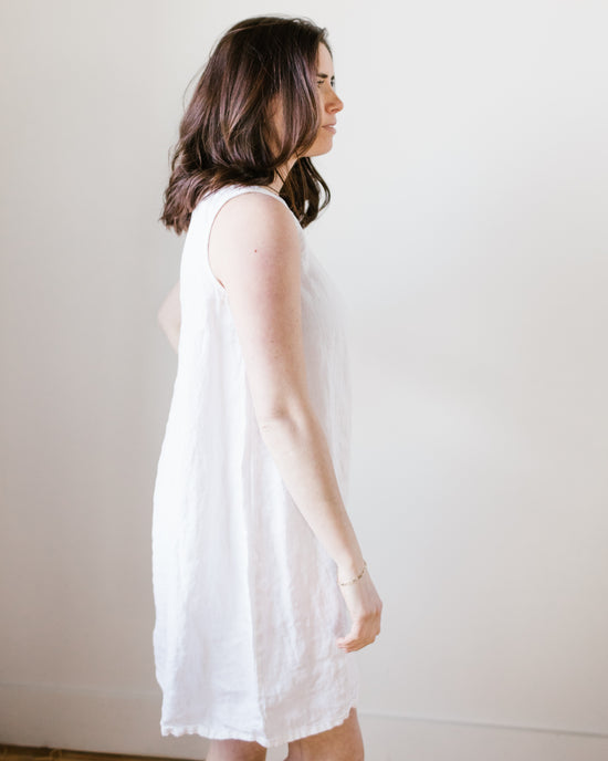 Woman standing in profile wearing a CP Shades Jess Dress in White HW Linen Twill against a plain background.