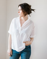 Woman in a Delilah - Cabo in White popover blouse with double button cuff and jeans standing against a light background.