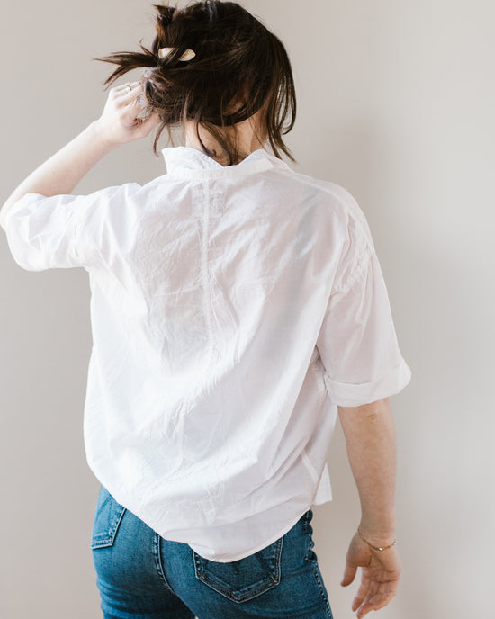 Woman in a Delilah - Cabo in White drop shoulder popover blouse from A Shirt Thing and blue jeans tying her hair up.