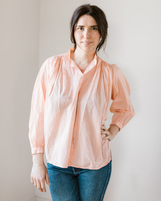 Woman in a long sleeve, light coral Flora - Cabo in Powder button-down shirt by A Shirt Thing and blue jeans standing against a plain background.