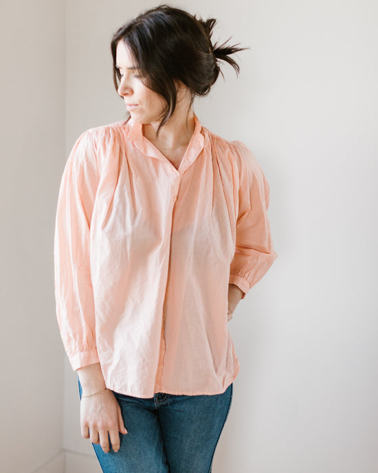 Woman in a "Flora - Cabo in Powder" long sleeve button-down shirt by A Shirt Thing and blue jeans looking to the side with hair blowing.