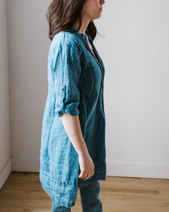 A woman in a CP Shades Regina in Bleach Indigo Twill tunic and jeans standing in profile against a neutral background.