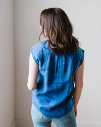A woman in a sleeveless Hartford Cleo Shirt in Mykonos and denim jeans standing with her back to the camera against a neutral background.