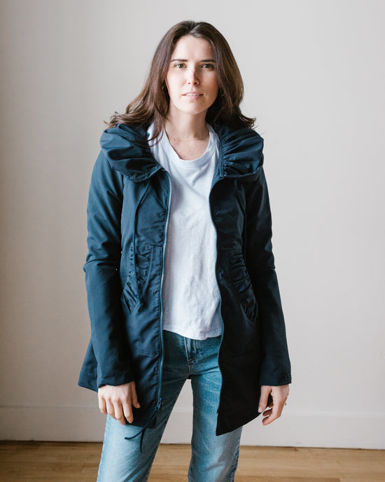 Woman standing against a light-colored background wearing a Prairie Underground Mid Raincoat in Navy, white t-shirt, and jeans.
