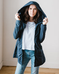 Woman in Prairie Underground Mid Raincoat in Navy and DWR coated poly jeans standing against a neutral background.
