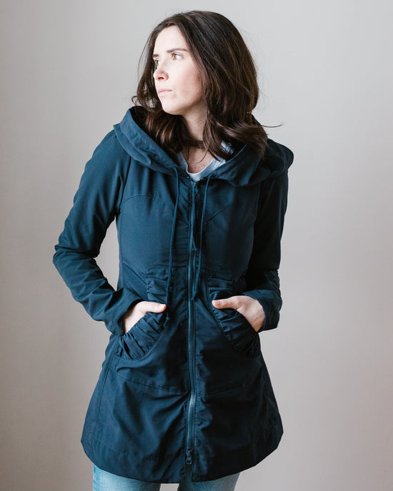 Woman standing with hands in pockets, wearing a Victorian-style Mid Raincoat in Navy by Prairie Underground and looking to the side.