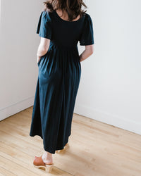Woman standing in a room wearing a Demylee Elana Dress in Navy and tan shoes.