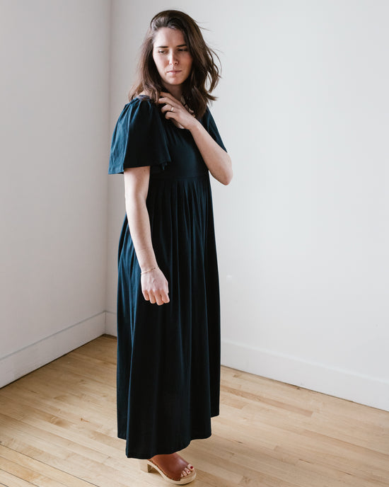 Woman in a Demylee Elana Dress in Navy standing in a room with light walls.