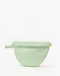 A pale green Grande Fanny in Mist Woven Checker leather handbag with a gold buckle and a detachable strap, displayed against a white background by Clare V.