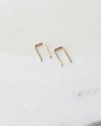 Two small metal staples on a white surface, replicating Token Jewelry's Mini Staple Earrings in 14K Gold Fill.
