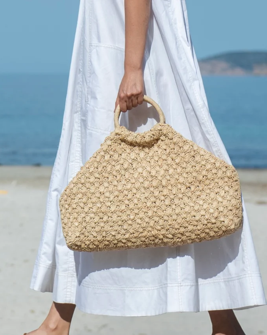 A person holding a 100% Natural Clementine Bag by Maison N.H. Paris while walking on the beach.