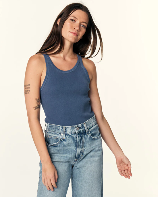 Woman in a long rib tank top made of 100% cotton in Deep Indigo by AMO and jeans posing against a light background.