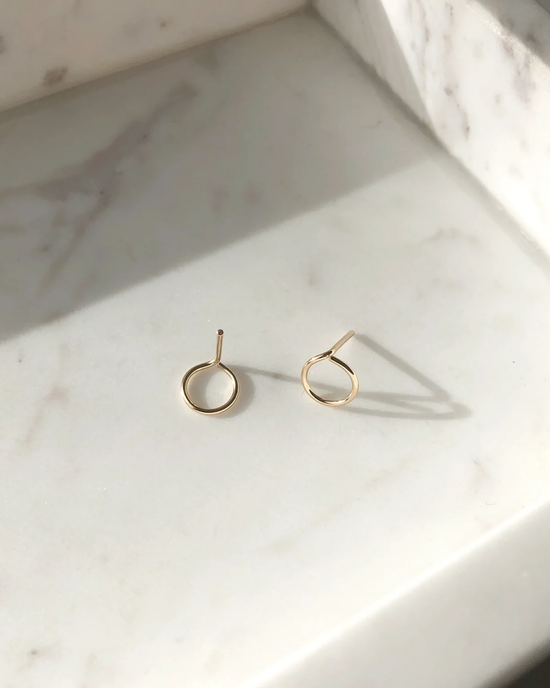 A pair of Token Jewelry Loop Earrings in 14K Gold Fill on a marble surface.