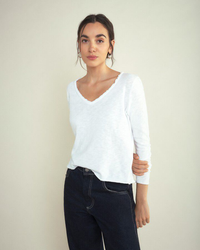 Woman in an American Vintage Sonoma L/S V in Blanc top and dark jeans posing against a neutral background.