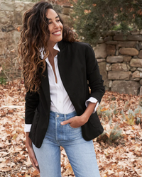 A woman smiling outdoors wearing a black Dublin Tailored Blazer in Jet Black Denim by Frank & Eileen, white shirt, and blue jeans made of lightweight cotton denim.