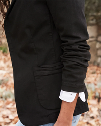 A close-up of a person wearing a Frank & Eileen Dublin Tailored Blazer in Jet Black Denim, featuring pocket detail, standing in an outdoor setting.