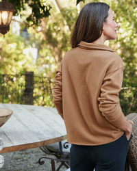 A woman seen from behind wearing a brown Patrick Henley in Camel Terry sweatshirt with a high collar, looking to the side in an outdoor setting by Frank & Eileen.