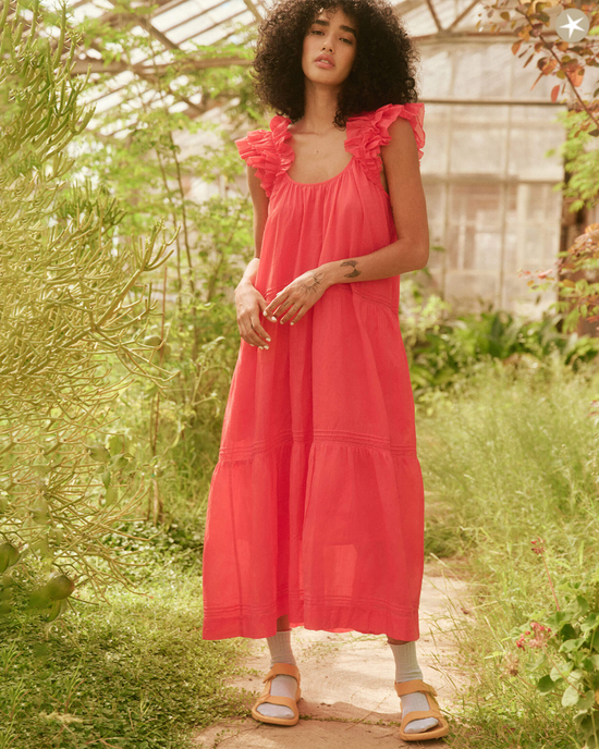 Woman in The Dove Dress in Tart by the Great, a lightweight cotton dress with ruffled shoulders, standing in a greenhouse.