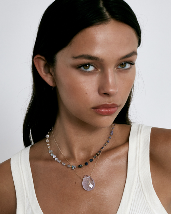 A woman with a neutral expression wearing a white sleeveless top and an 18k gold plated sterling silver Chan Luu Daphne Beaded Necklace in Iolite Mix.
