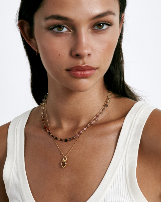Close-up of a woman wearing a white sleeveless top and an 18k gold plated sterling silver Chan Luu Daphne Beaded Necklace in Citrine Mix with a pendant.