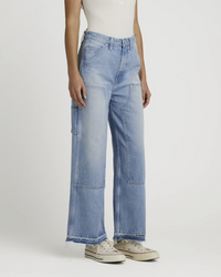 Woman standing in light-wash Edwin Nova Carpenter Ankle jeans in Escapade with frayed detail.