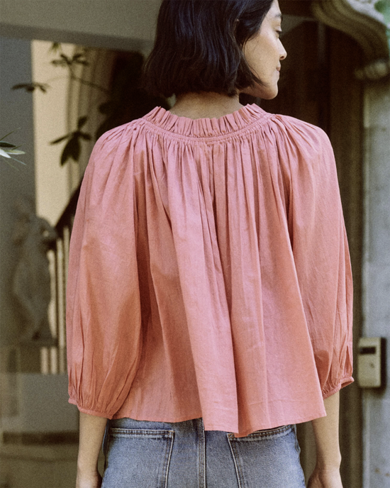 Woman in a peach blouse with an elastic ruffled neckline seen from behind, wearing The Prim Top in Cherry Blossom by the Great.