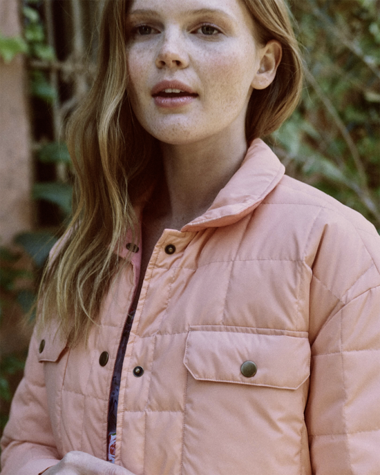 Woman in a light pink The Reversible Cloud Puffer jacket by the Great, standing outdoors.