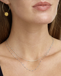 A woman wearing a delicate Chan Luu CL NG-14371 Necklace in Stone Blue and gold hoop earring.