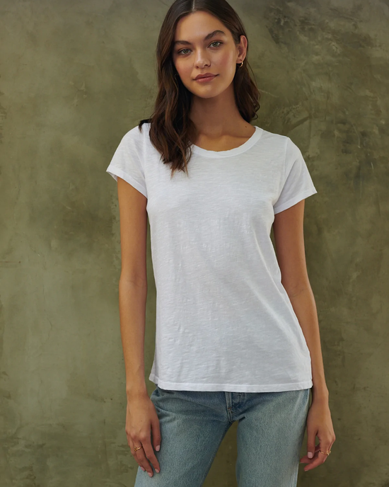Woman posing in a white Velvet by Graham & Spencer Tilly Tee Shirt and blue jeans against a textured background.