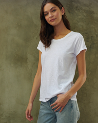 Woman in a white crew neck Velvet by Graham & Spencer Tilly Tee Shirt posing with hand in pocket against a textured grey background.