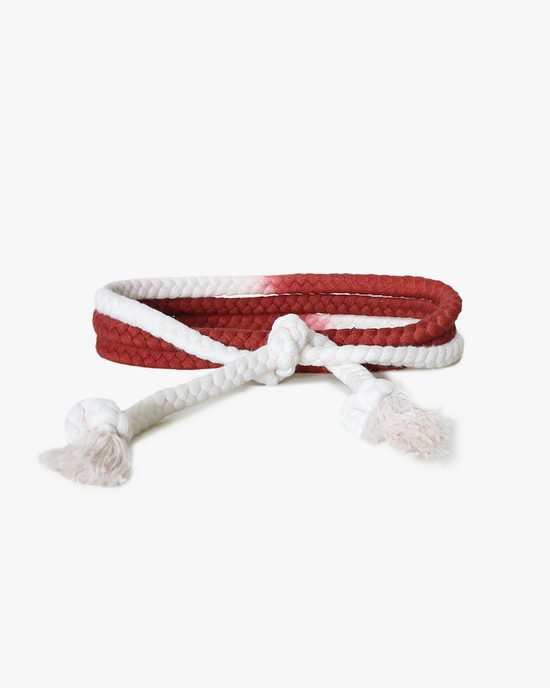 A red and white ombre dip dye braided XiRENA Rope Belt in Redwood dog toy with knotted ends.