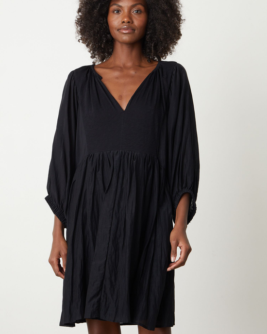 A woman in a Velvet by Graham & Spencer Erin Shirred Waist L/S Dress in Black with a v-neckline and long sleeves.