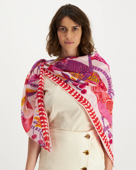 Woman wearing a beige dress and an oversized, colorful fish-patterned scarf from Inoui Editions, featuring the Square 130 Cerise in Pink design.