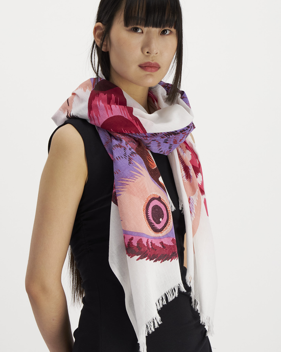Woman posing with the Inoui Editions Scarf 100 Toucan in Pink, a 100% cotton, colorful scarf with a fringe, against a white background.