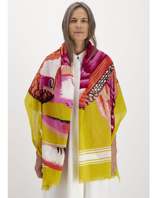 Woman wearing an Inoui Editions Scarf 100 Toucan in Yellow over a white garment, standing against a neutral background.