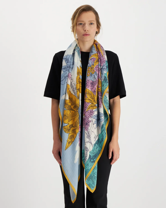 A woman wearing a black shirt and an Inoui Editions Square 130 Robinson in Blue silk cashmere blend floral print oversized bandana.