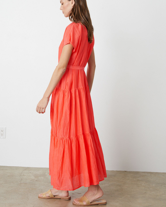 Woman wearing a Coral red cotton Ada Flounce Tier Dress in Dolly by Velvet by Graham & Spencer, with short sleeves and sandals, standing in profile view.