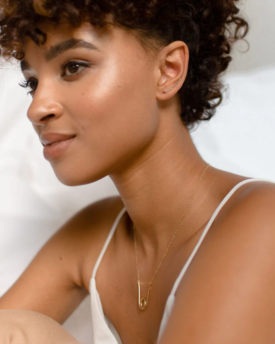 Close-up portrait of a woman with curly hair wearing handmade jewelry, including a delicate necklace and Token Jewelry's Ear Climbers in 14K Gold Fill.