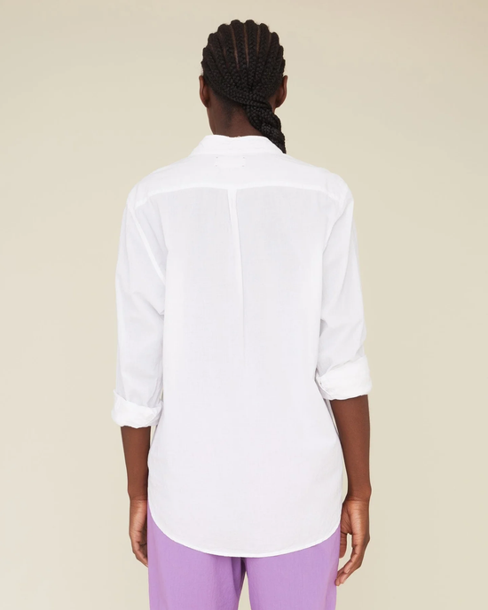 A person standing with their back to the camera, wearing a XiRENA Beau Top in White and purple pants.